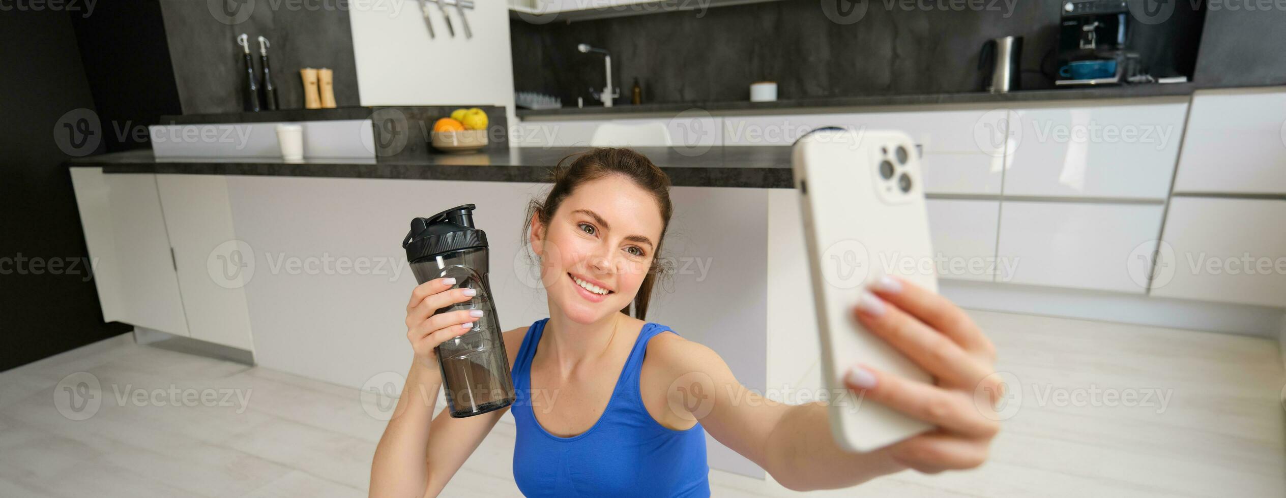 bienestar y Deportes. hermosa joven mujer tomando selfie en teléfono inteligente, haciendo aptitud formación desde hogar, bebida agua, corsé hidratado y haciendo ejercicios foto