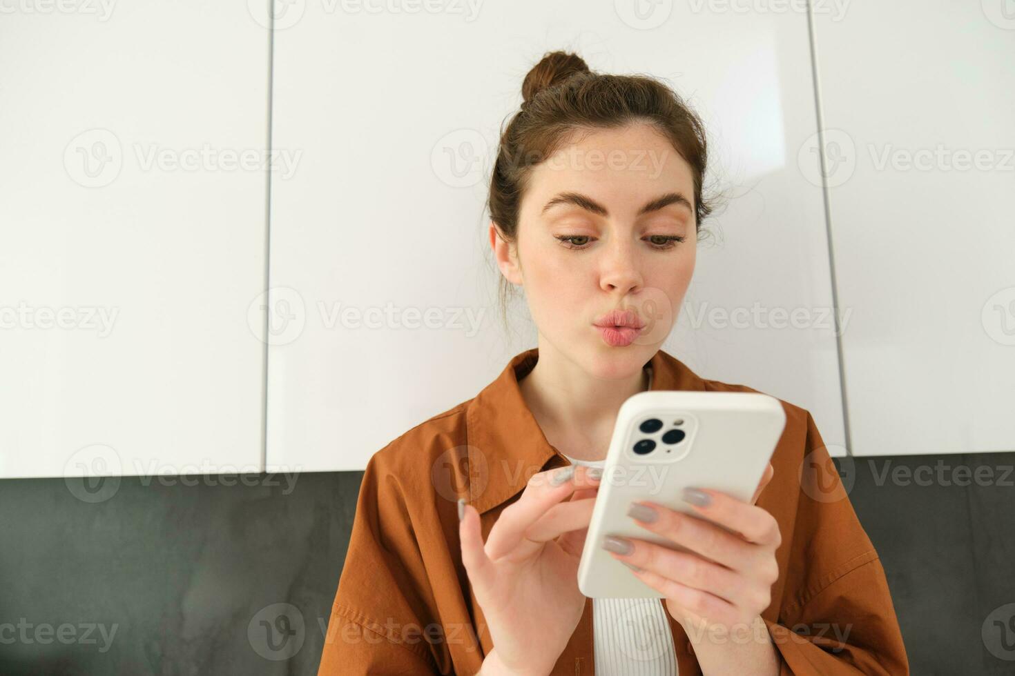 Portrait of young woman at home, looking with interest at smartphone screen, concept of online shopping, buying on mobile apps, picking something using application on phone photo