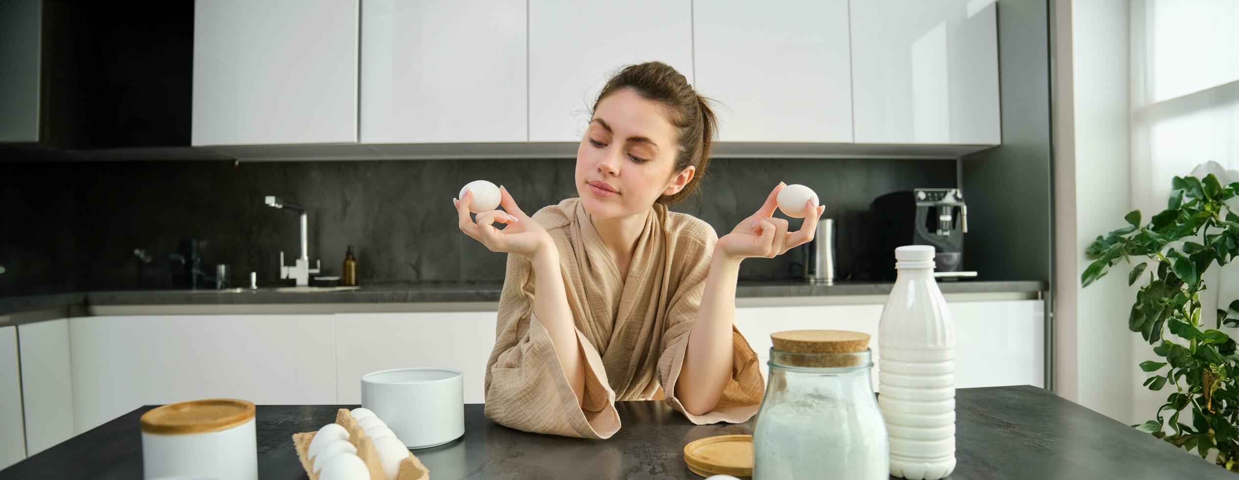 Attractive young cheerful girl baking at the kitchen, making dough, holding recipe book, having ideas photo