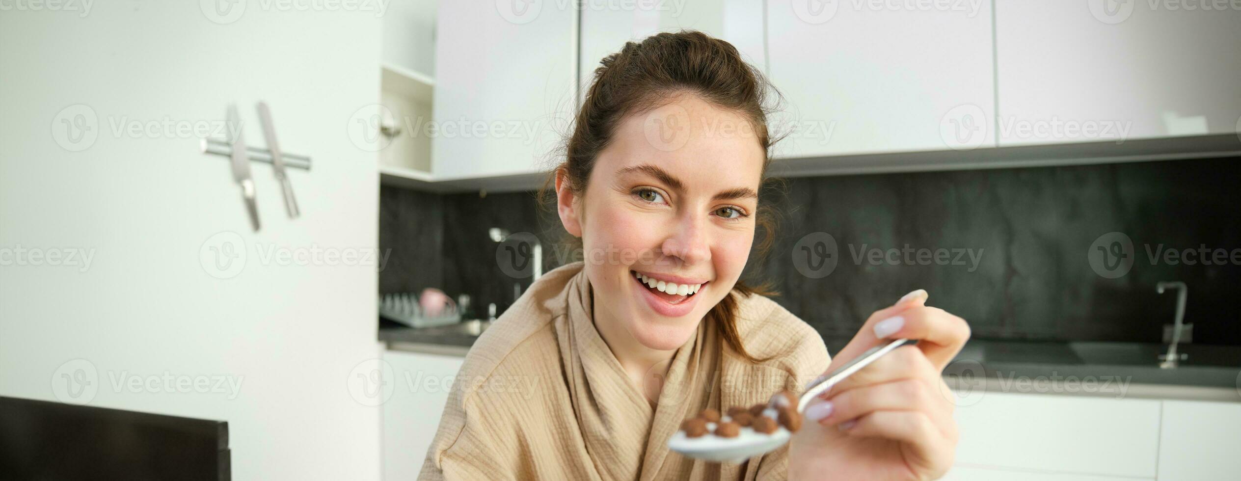 Close up of beautiful woman feeding you cereals, having breakfast with milk, smiling and laughing, leaning on kitchen worktop photo