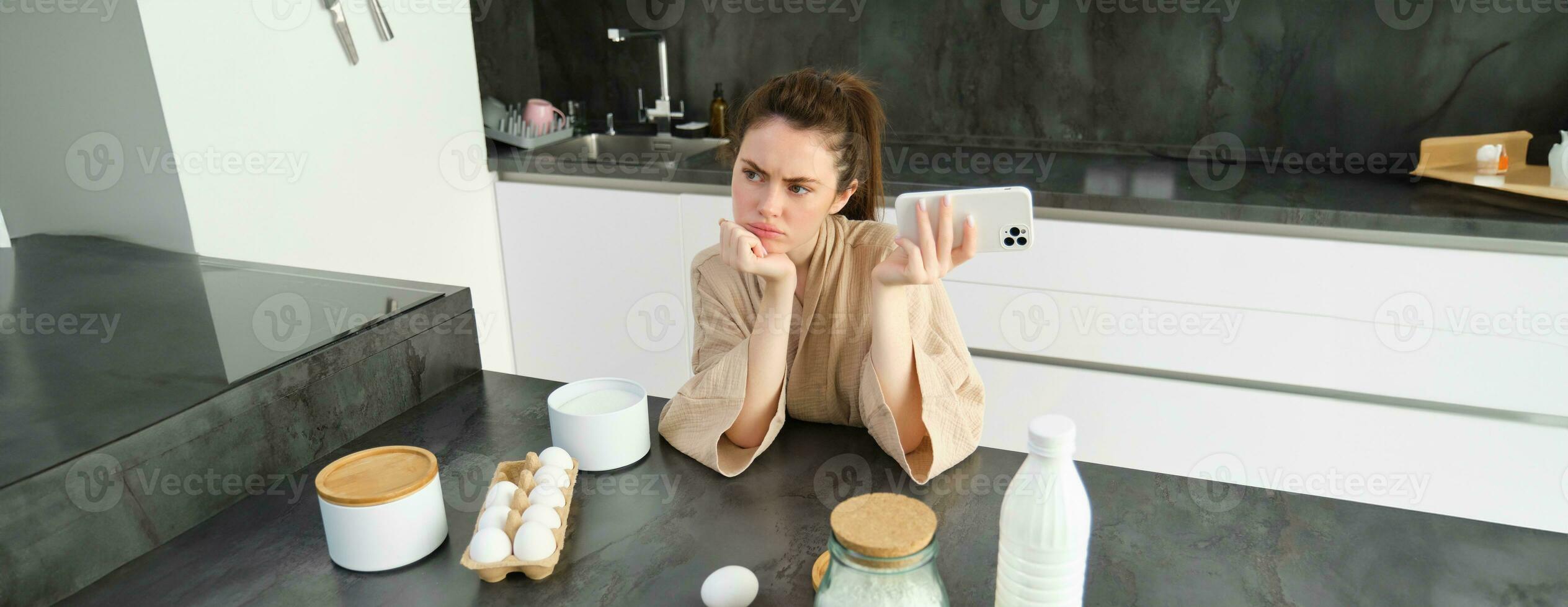 atractivo joven alegre niña horneando a el cocina, haciendo masa, participación receta libro, teniendo ideas foto