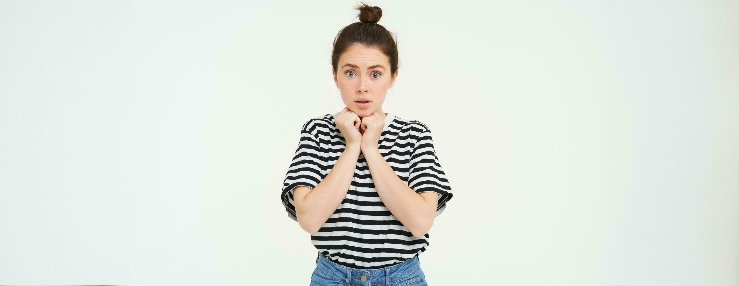 Portrait of young compassionate woman, looking with sympaty, gasping at camera, raising eyebrows, standing over white background photo