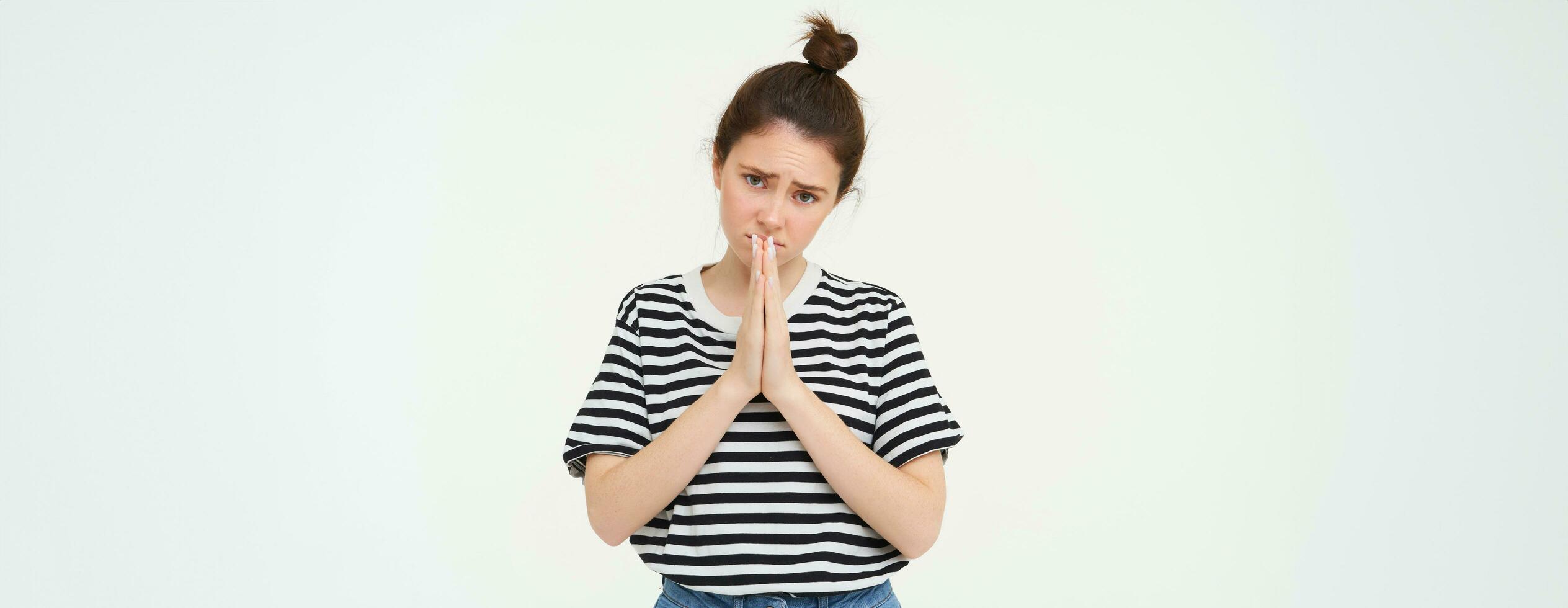 Please. Young woman asks for help, begs you, holds hands in pray, pleading, isolated against white background photo