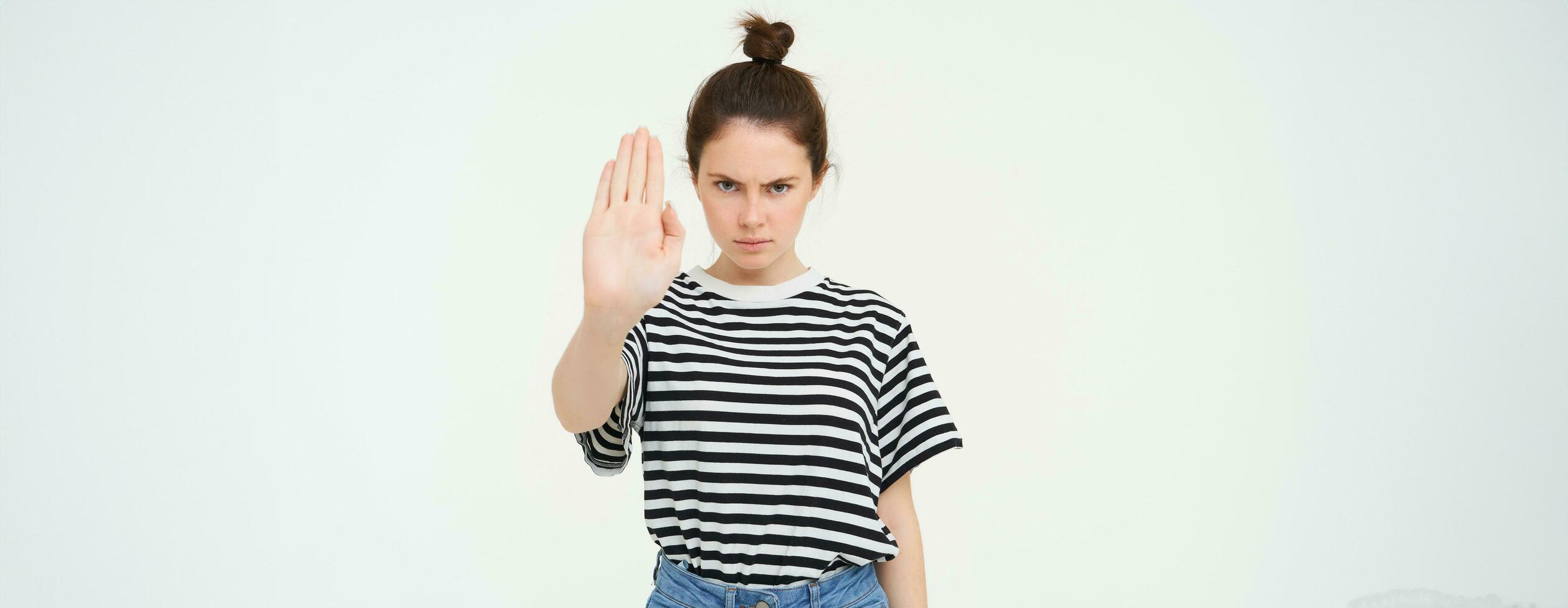 Image of serious and confident young woman, shows stop sign, taboo gesture, prohibit something bad, standing over white background photo