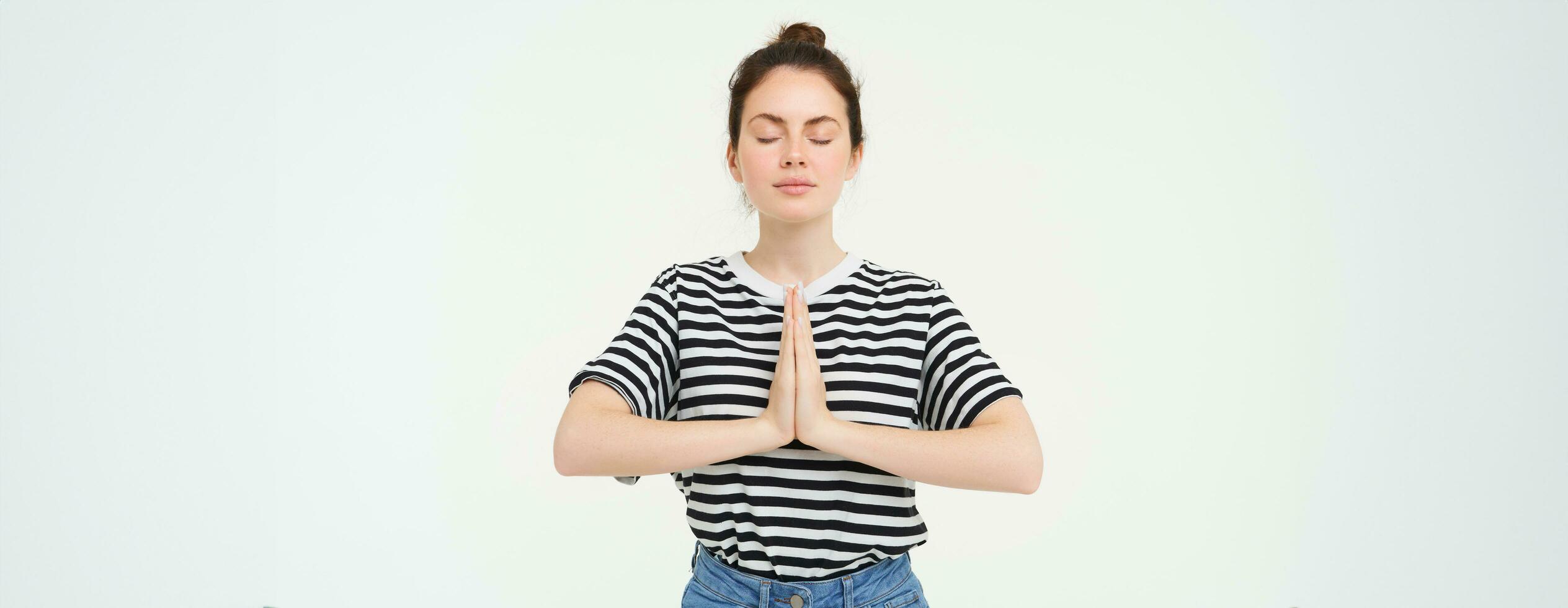 retrato de joven consciente de mujer meditando, sostiene manos abrochado juntos, namaste gesto, práctica yoga, en pie terminado blanco antecedentes foto
