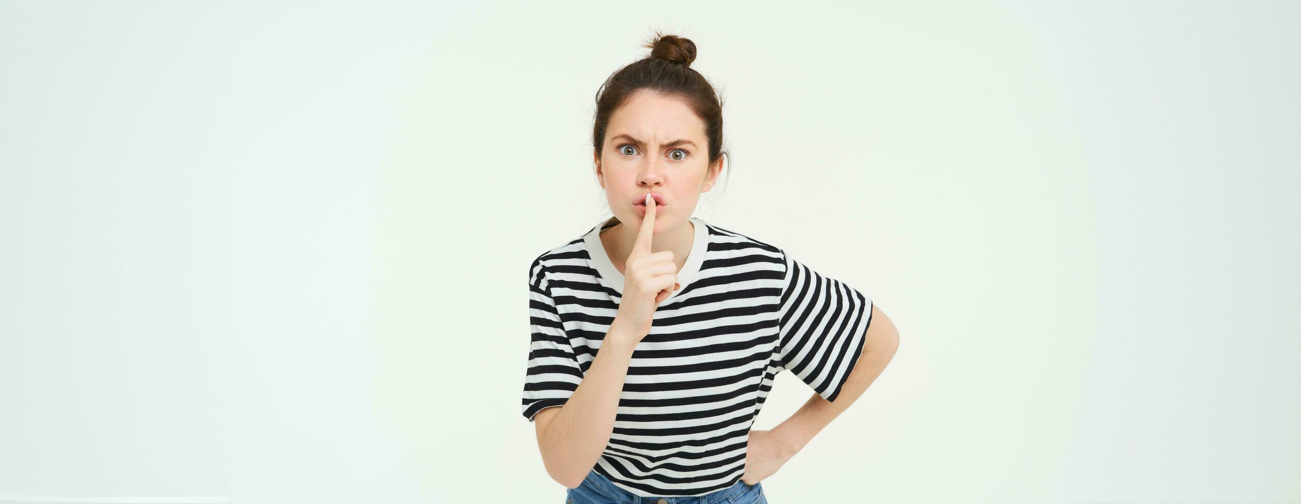 Angry woman shushing, hush at you, press finger to lips, tells to keep quiet, arguing, scolding someone, standing over white background photo