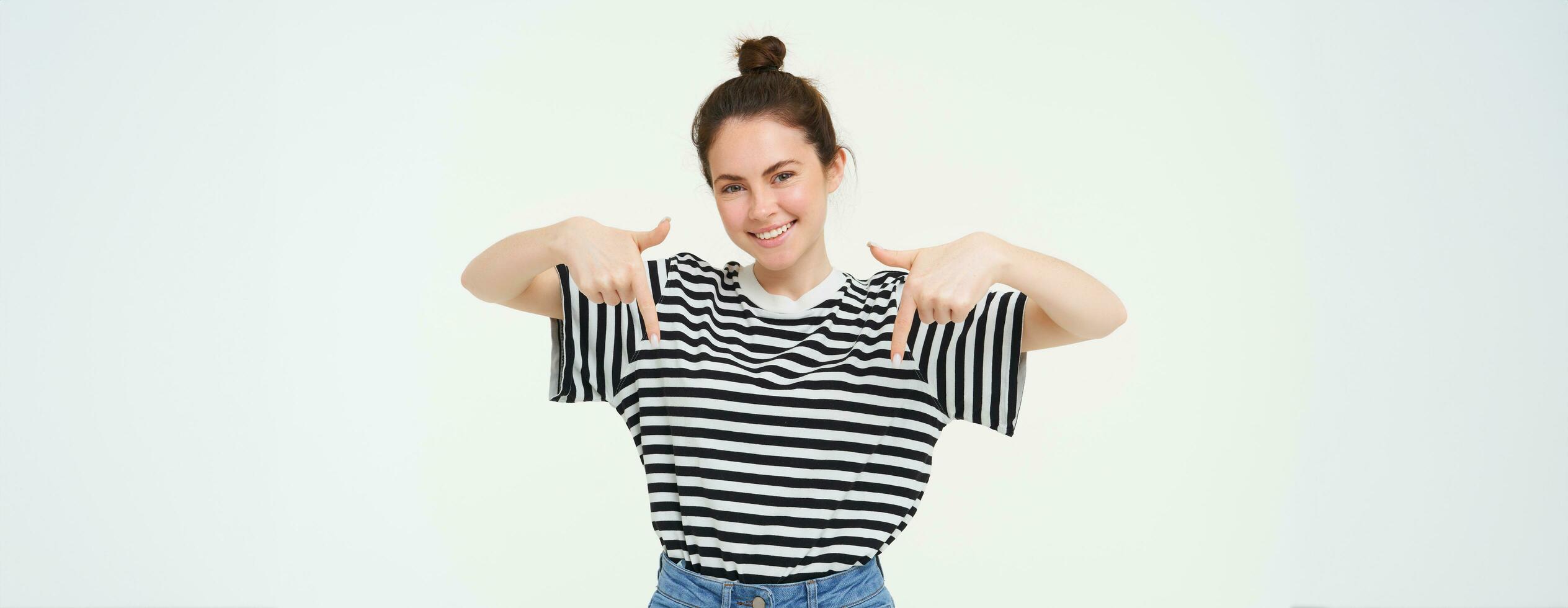 retrato de hermoso, sonriente joven hembra modelo, demostración anuncio publicitario, señalando dedos abajo, en pie terminado blanco antecedentes foto