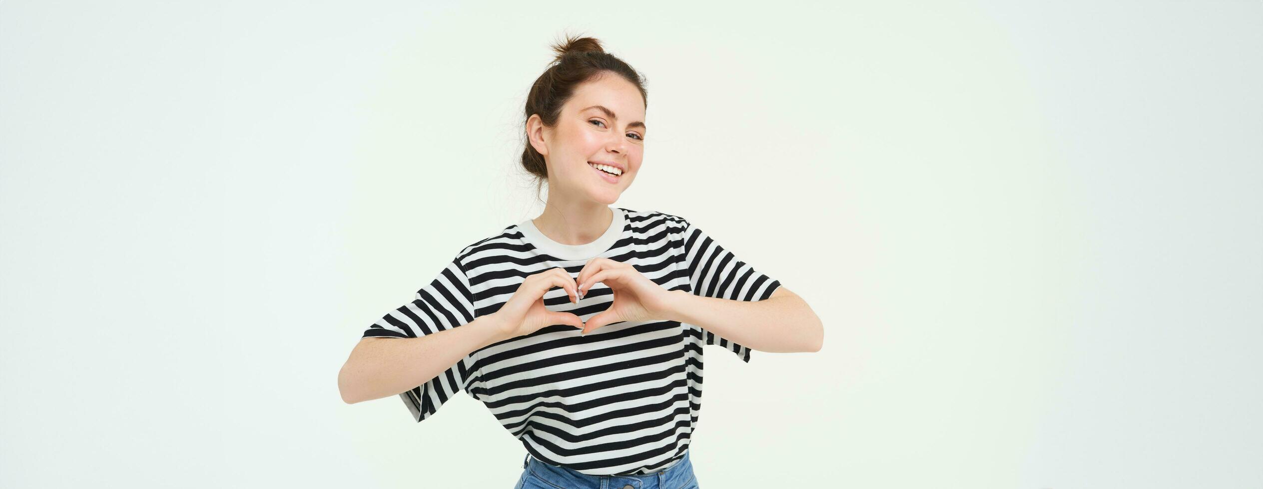 Portrait of beautiful girl shows heart sign, love gesture, like something, stands over white background photo