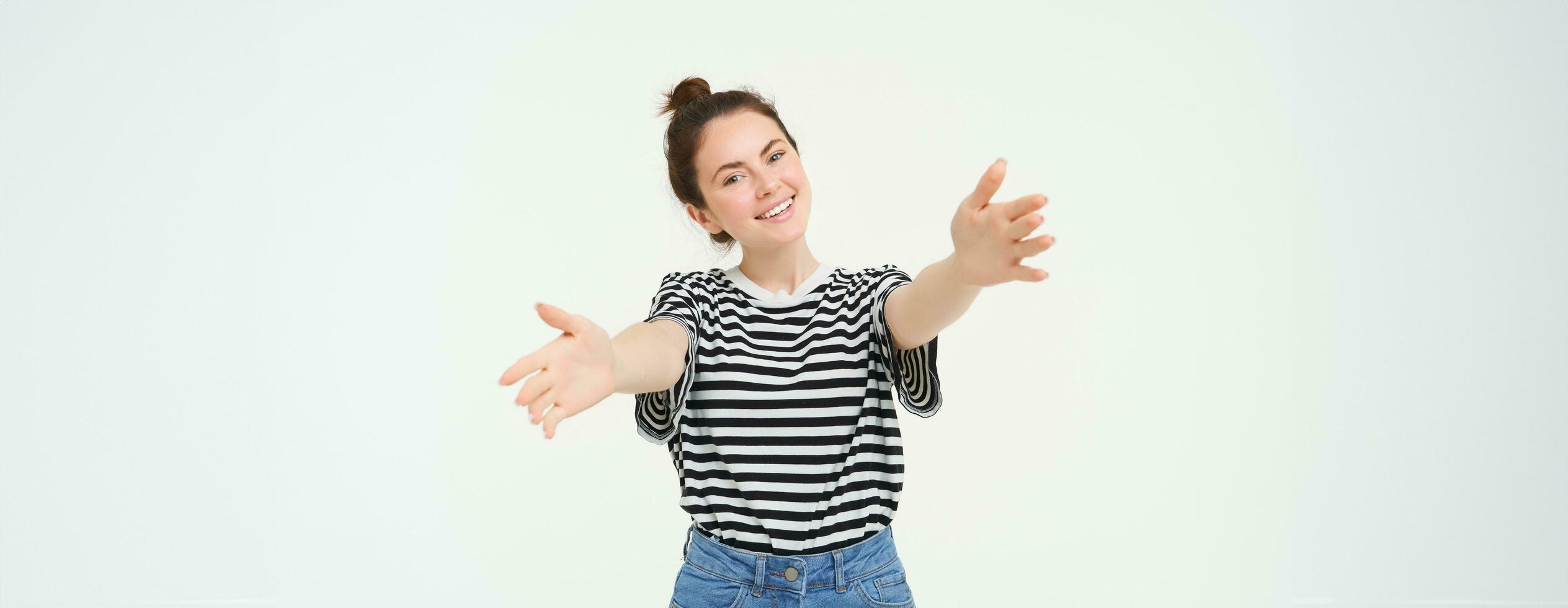 Portrait of smiling young woman reaching her hands, hugging you, wants to cuddle, stretching arms to receive, take smth, standing over white background photo