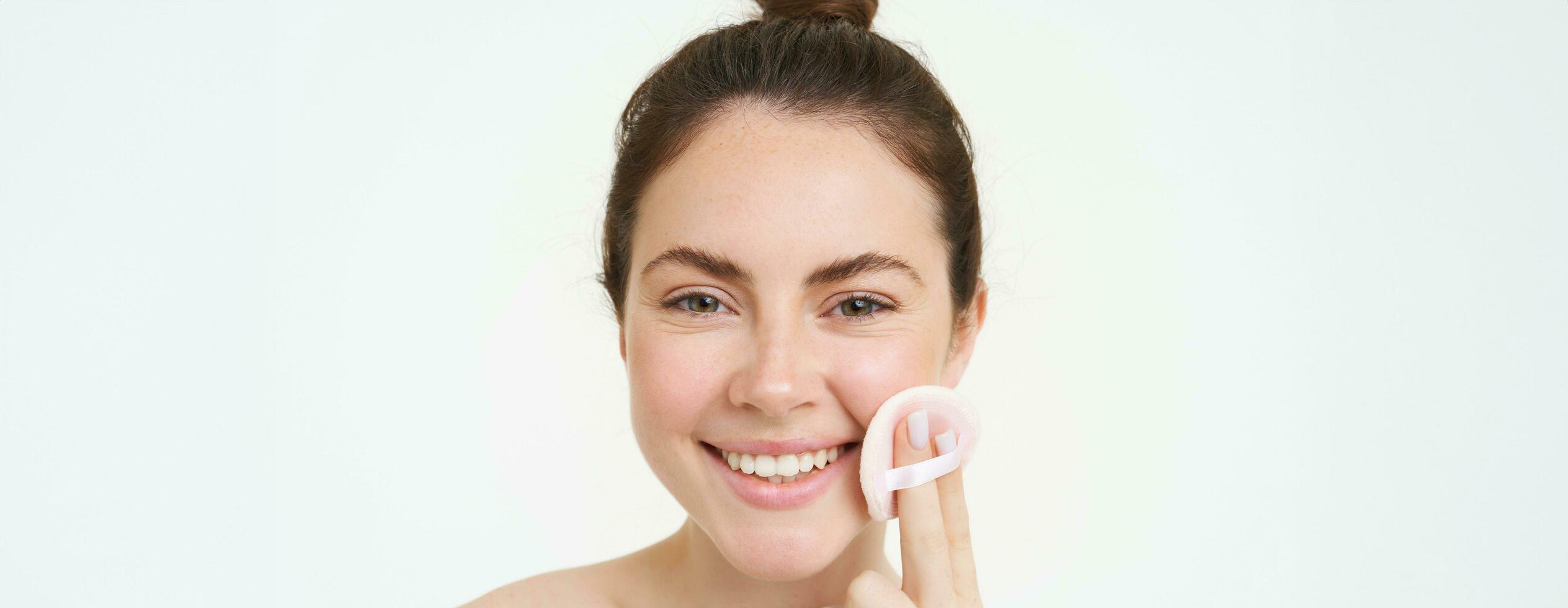Portrait of smiling happy woman without blemishes, using cosmetic pad to clean her face, using skincare routine treatment, facial toner, takes off makeup with cleanser, stands over white background photo