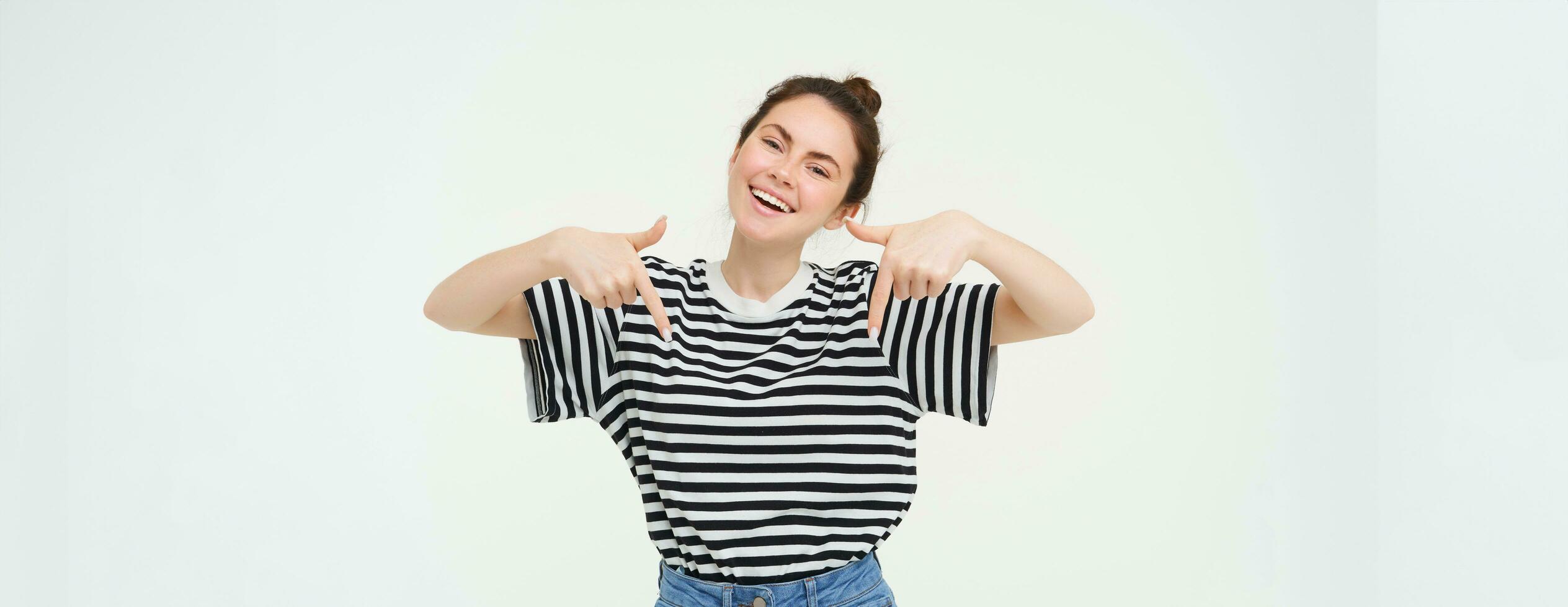 Enthusiastic girl points fingers down, shows advertisement, promo banner below, stands over white background photo