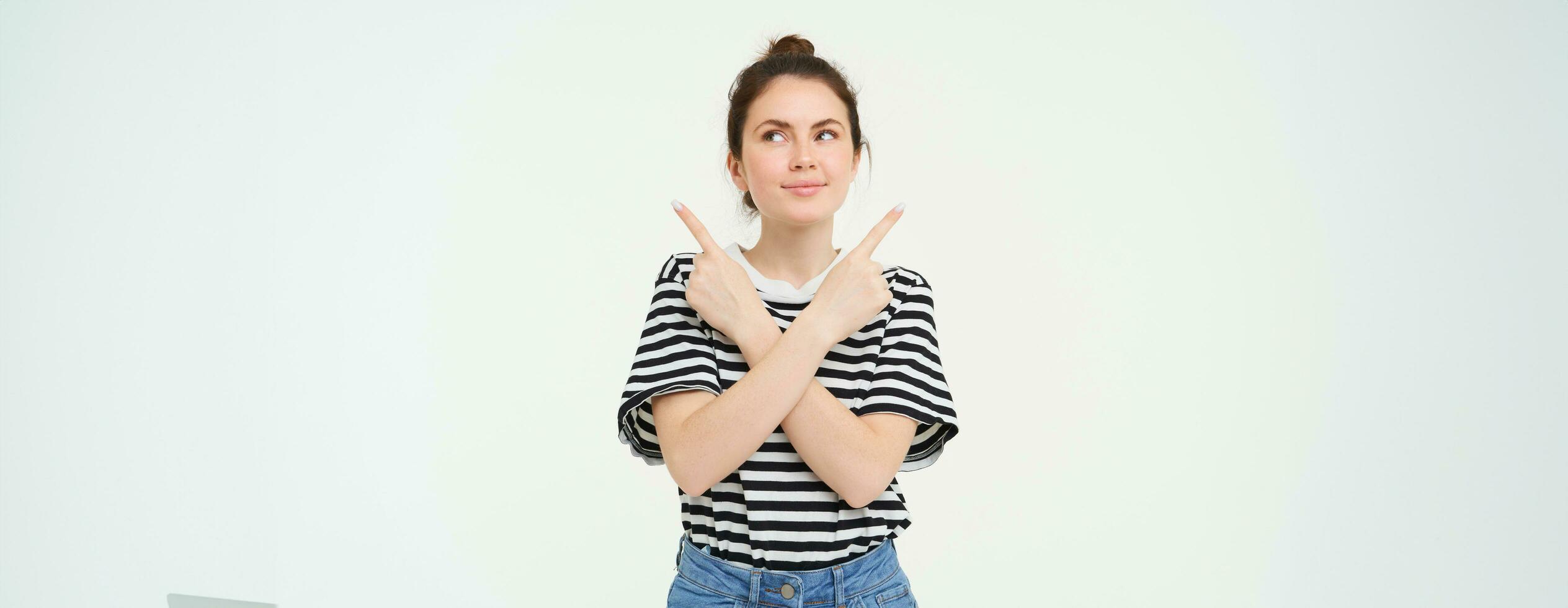 Portrait of beautiful, smiling young woman standing puzzled, makes choice, decides what to pick, points sideways left and right, stands over white background photo