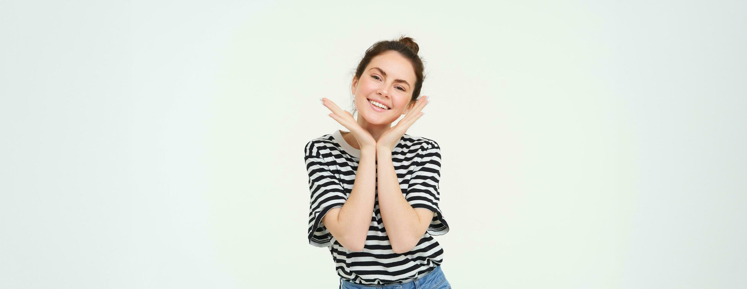 bienestar y mujer concepto. retrato de joven mujer con linda rostro, sostiene manos cerca cabeza y sonrisas, aislado en contra blanco antecedentes foto