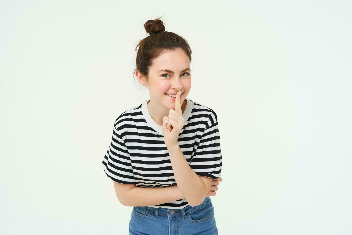 Beautiful, coquettish girl, holds finger on lips, promise to keep secret, shh gesture, hush sign, stands over white background photo