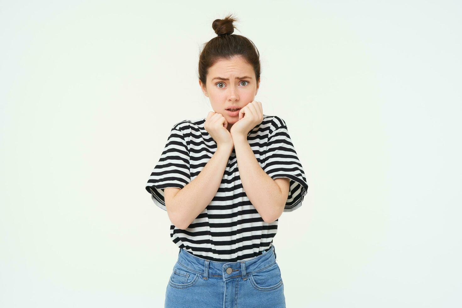 Portrait of scared, timid young woman, gasping, shaking from fear, looks frightened, stands over white background photo