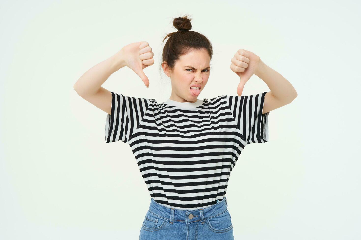 Young woman gives negative feedback, shows thumbs down, disapproves product, dislikes smth bad, stands over white background photo