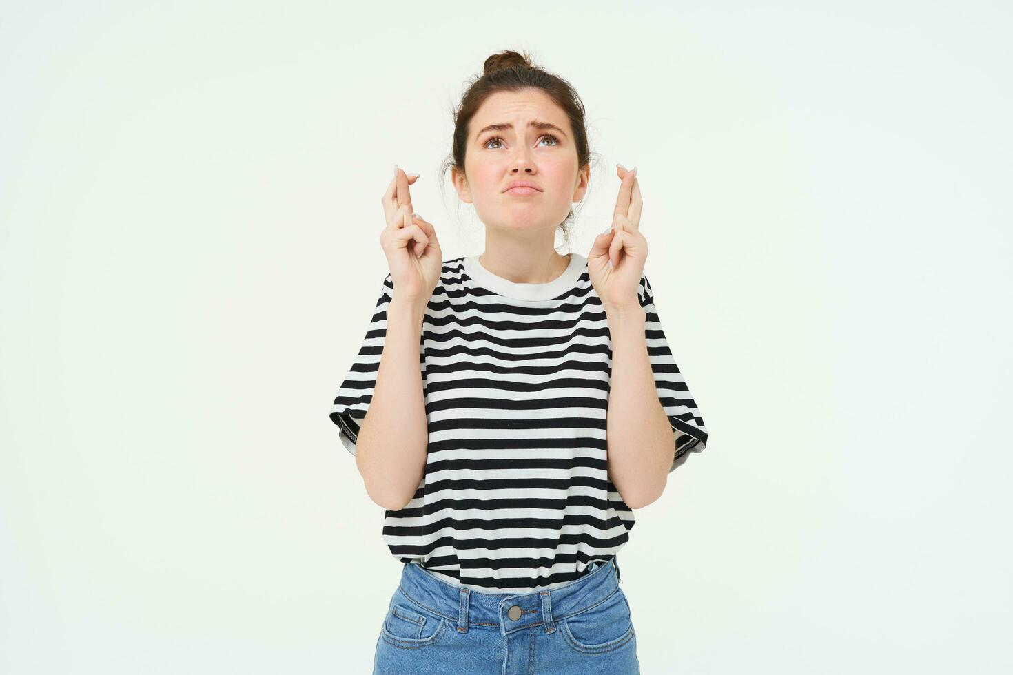 High hopes. Young woman cross fingers, makes wish, anticipates something, stands over white background photo