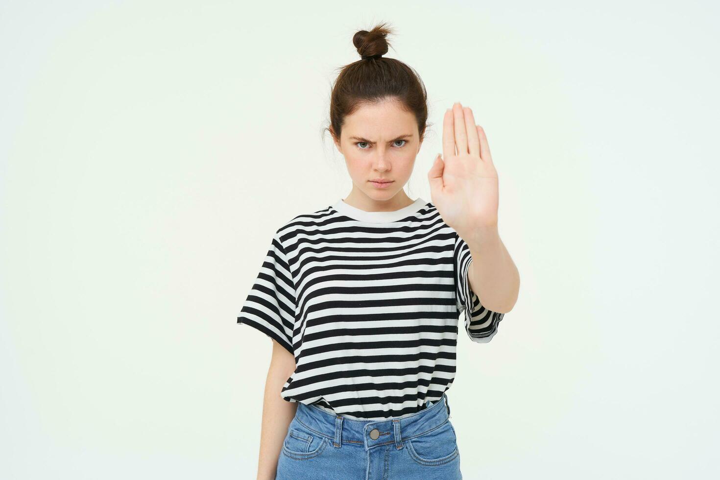 Image of serious and confident young woman, shows stop sign, taboo gesture, prohibit something bad, standing over white background photo