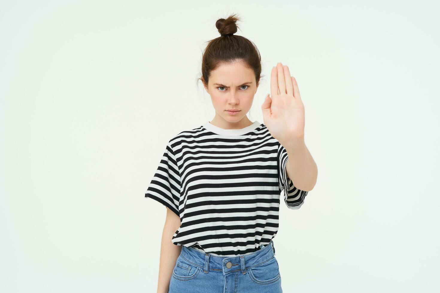 Image of serious and confident young woman, shows stop sign, taboo gesture, prohibit something bad, standing over white background photo