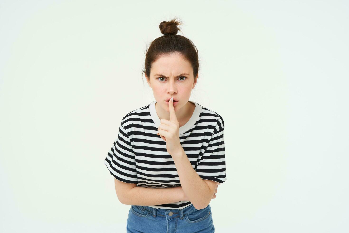 Image of angry woman shushing, makes hush gesture, press finger to lips with frustrated face, keep quiet, scolding loud person, white background photo
