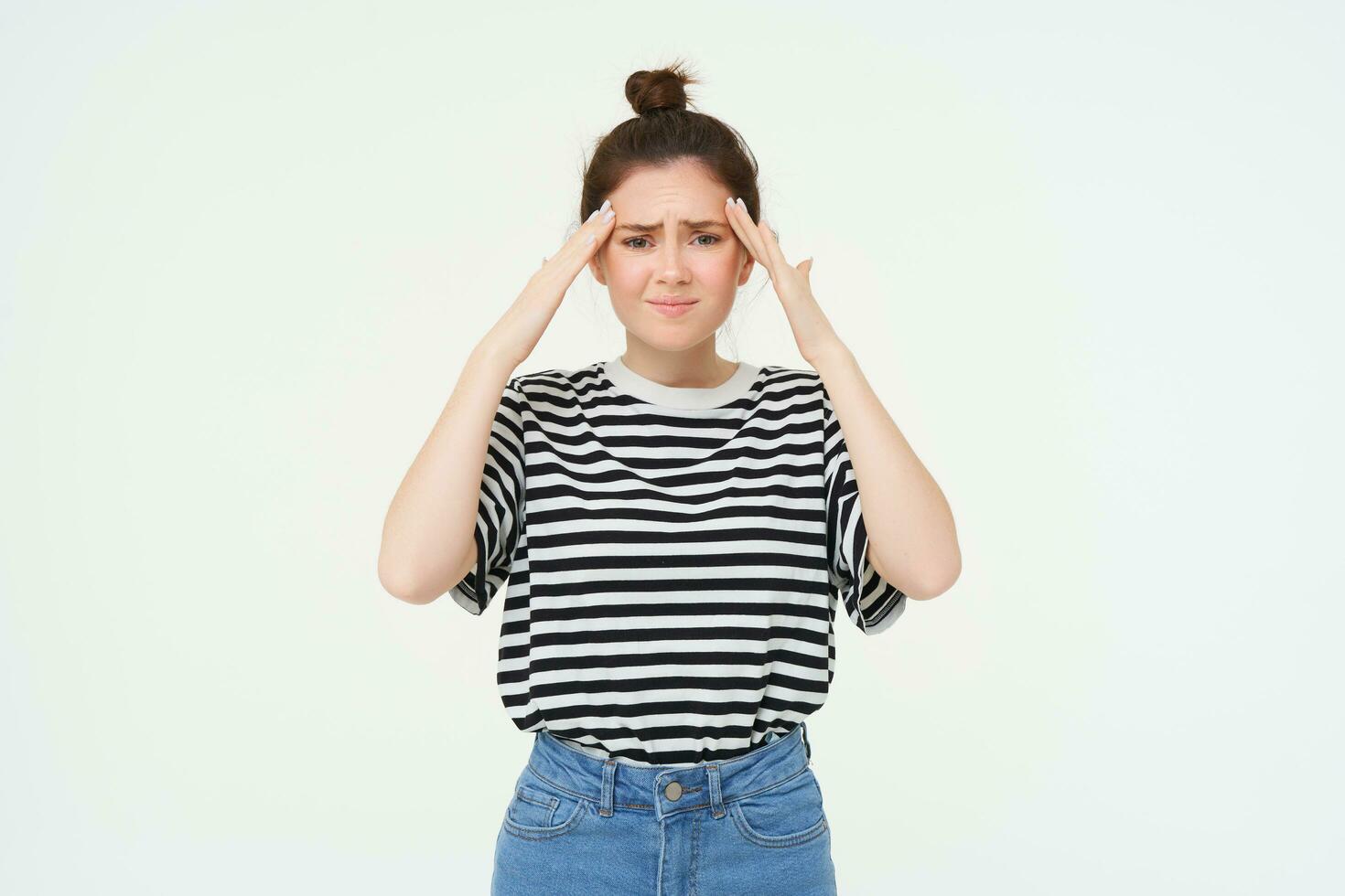 Portrait of woman with headache, touches her forehead and frowns from discomfort, stands over white background photo