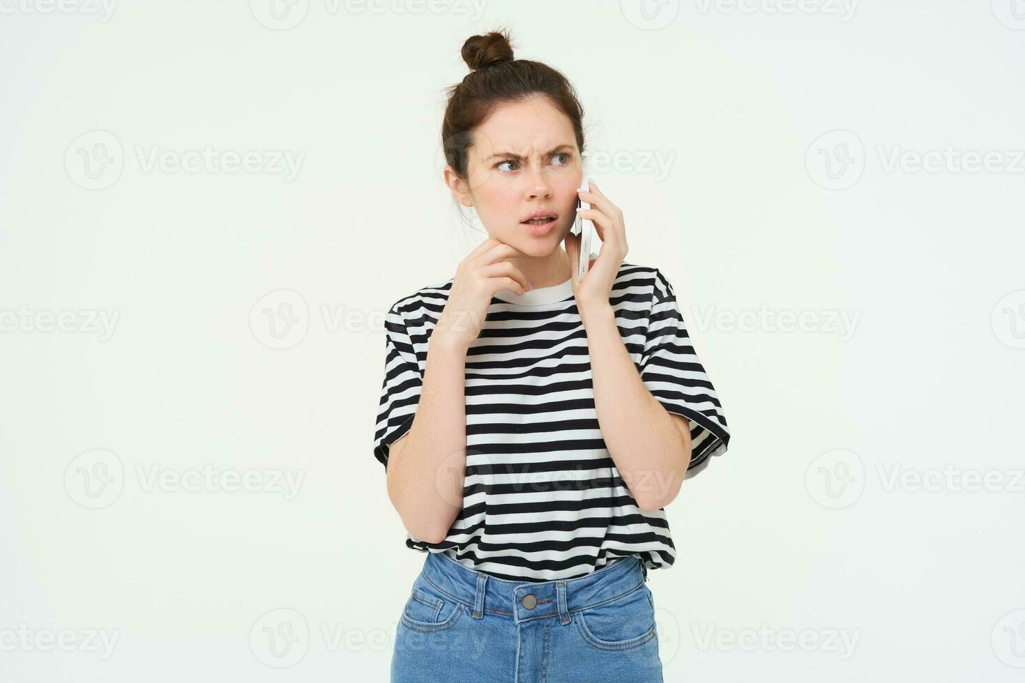 Image of woman with shocked face, looks confused while chats over the phone, listens to person on telephone, white background photo