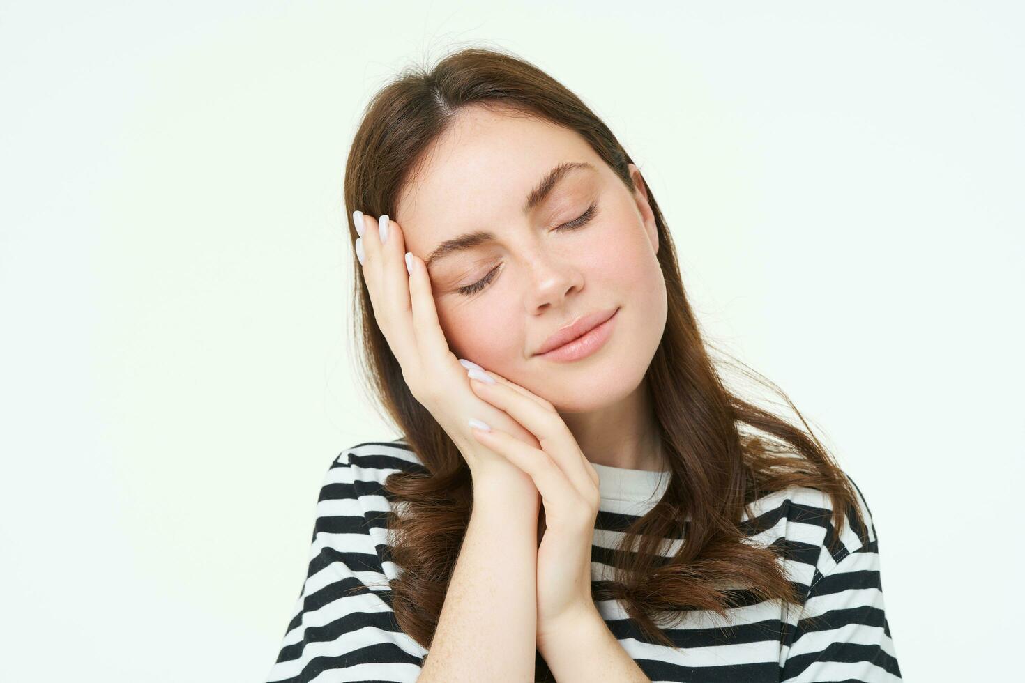 Close up portrait of tender, smiling young woman, closes her eyes and touches her palm, sleeping on her hand, isolated on white background photo
