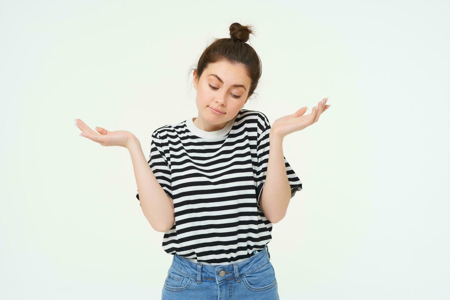 I dont know. Clueless young woman shrugging shoulders, looks confused, stands against white studio background photo