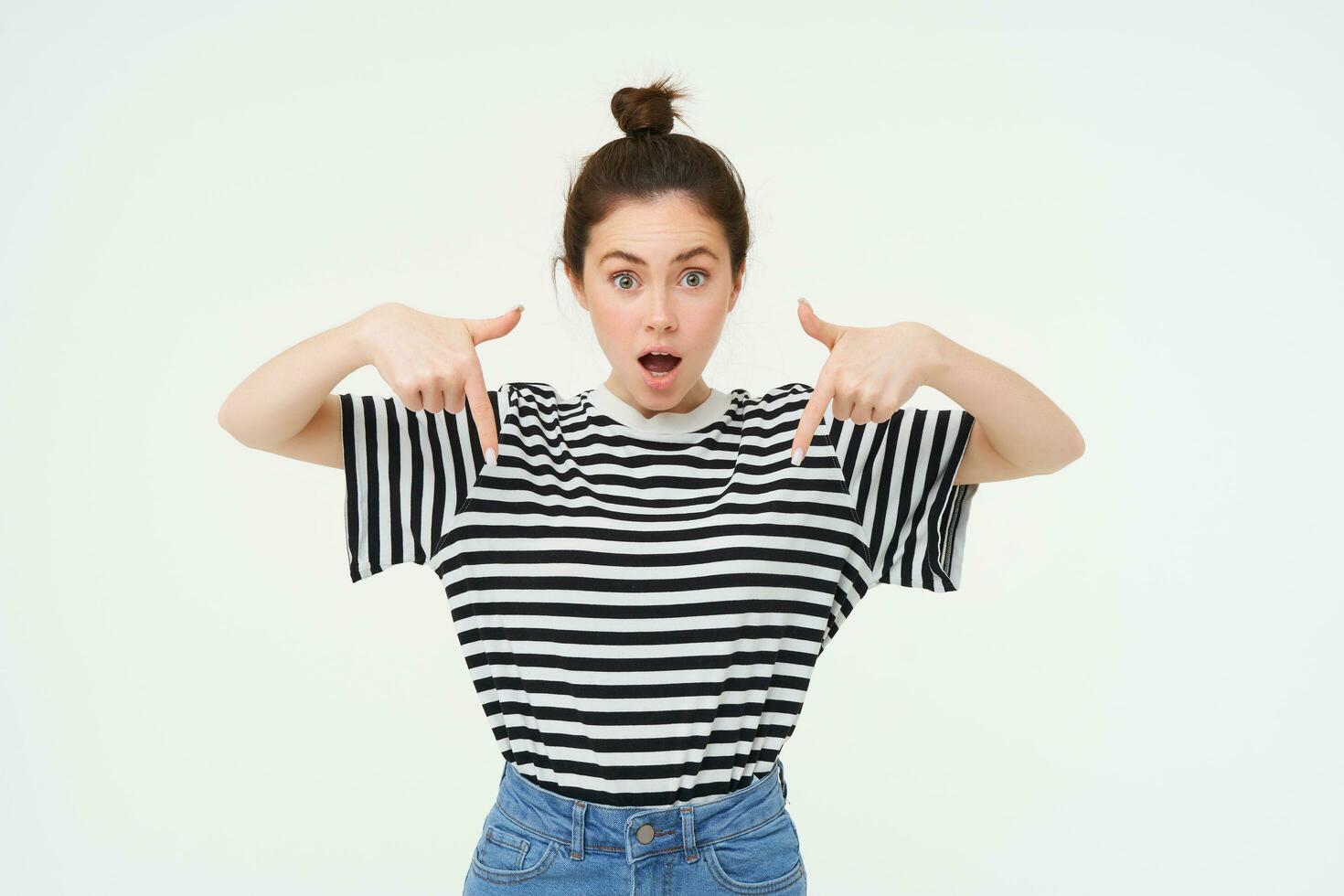 Image of impressed girl, drops jaw, says wow, points fingers down, shows advertisement, being amazed by awesome promo offer, white background photo