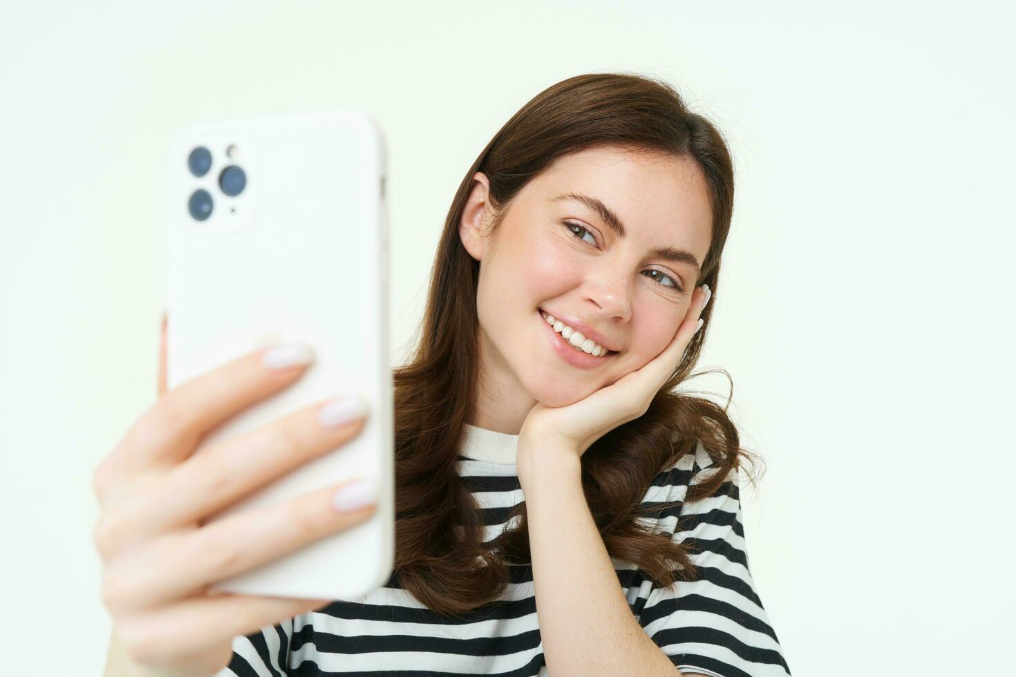 Portrait of young woman taking selfies on smartphone, posing for photo,. using mobile phone app for taking funny and cute pictures, isolated on white background photo