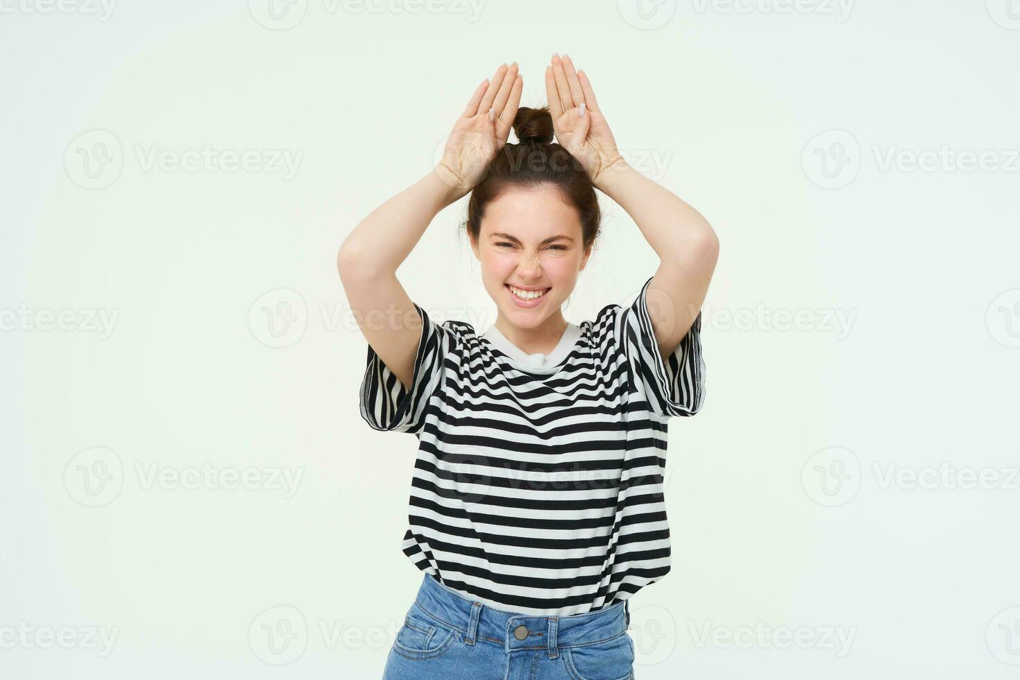 Image of beautiful, happy young woman showing bunny ears on top of her head, looking excited, posing over white background photo