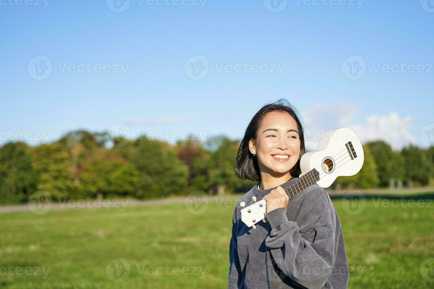 joven hipster chica, viajero participación su ukelele, jugando al aire libre en parque y sonriente foto