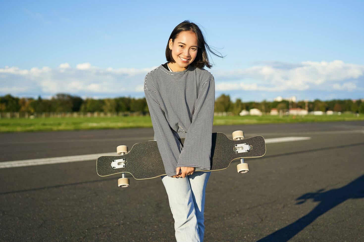 Portrait of beautiful asian girl skating on longboard, crusing with skateboard on empty road, enjoying freetime on fresh air photo
