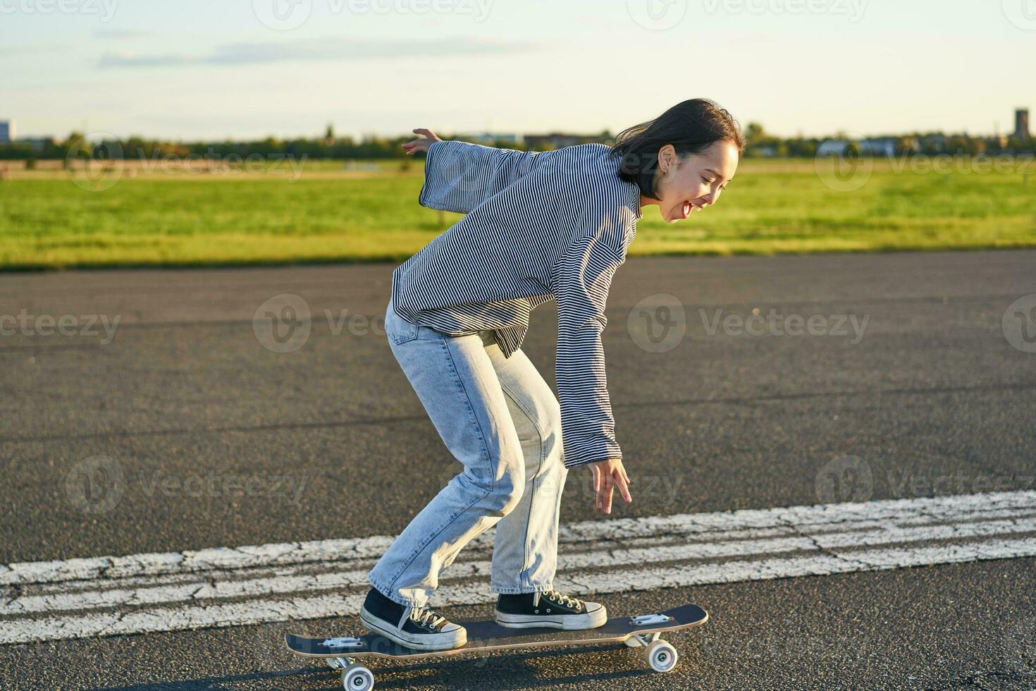 Happy skater girl riding her skateboard and having fun on empty street. Smiling woman enjoying cruiser ride on sunny road photo