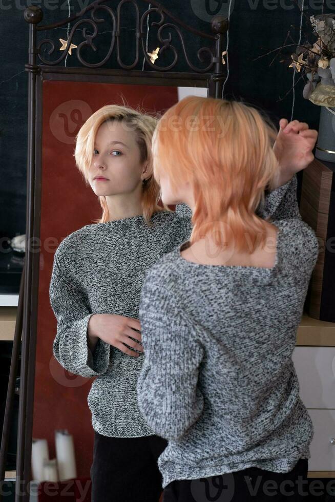 teenager girl looks in the mirror indoor, carefully examines her hairstyle photo