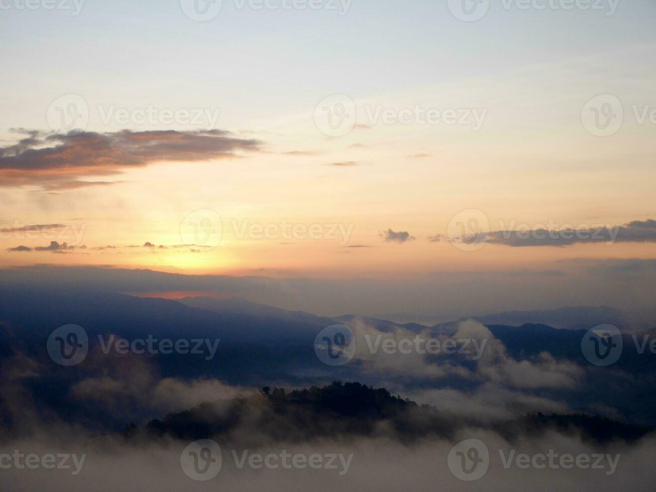 The mist flows through the mountain forest, Sun shining into tropical forest, Mist drifts through mountain ridges in the morning, slow floating fog blowing cover on the top of mountain photo