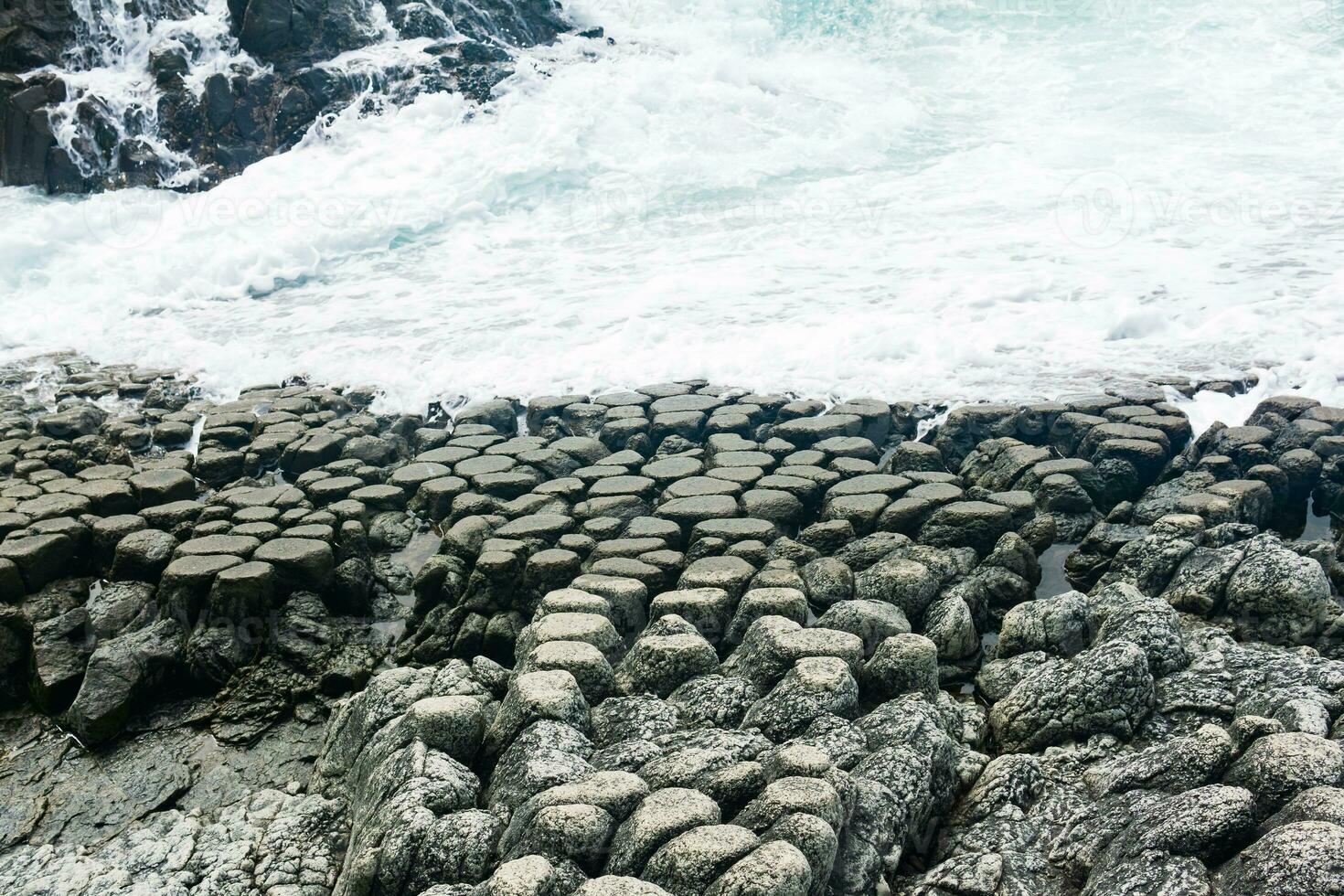 natural cobblestone causeway, formed by the ends of lava columns, descends into the sea surf photo