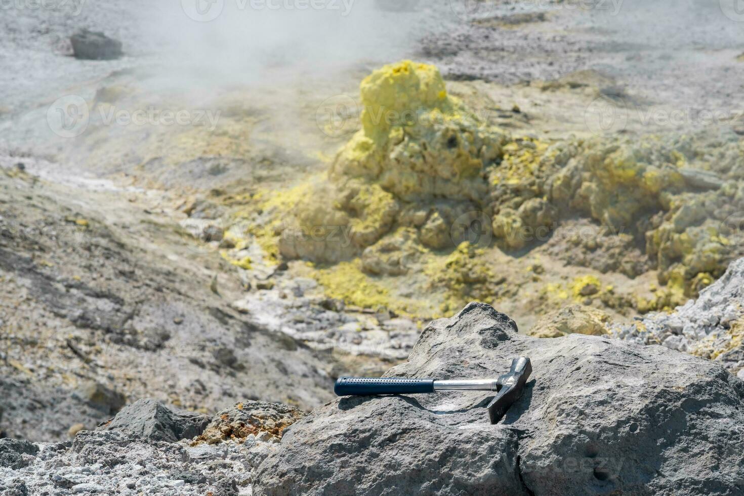 geological hammer on the rock against the backdrop of an steaming fumarole on the slope of a volcano photo