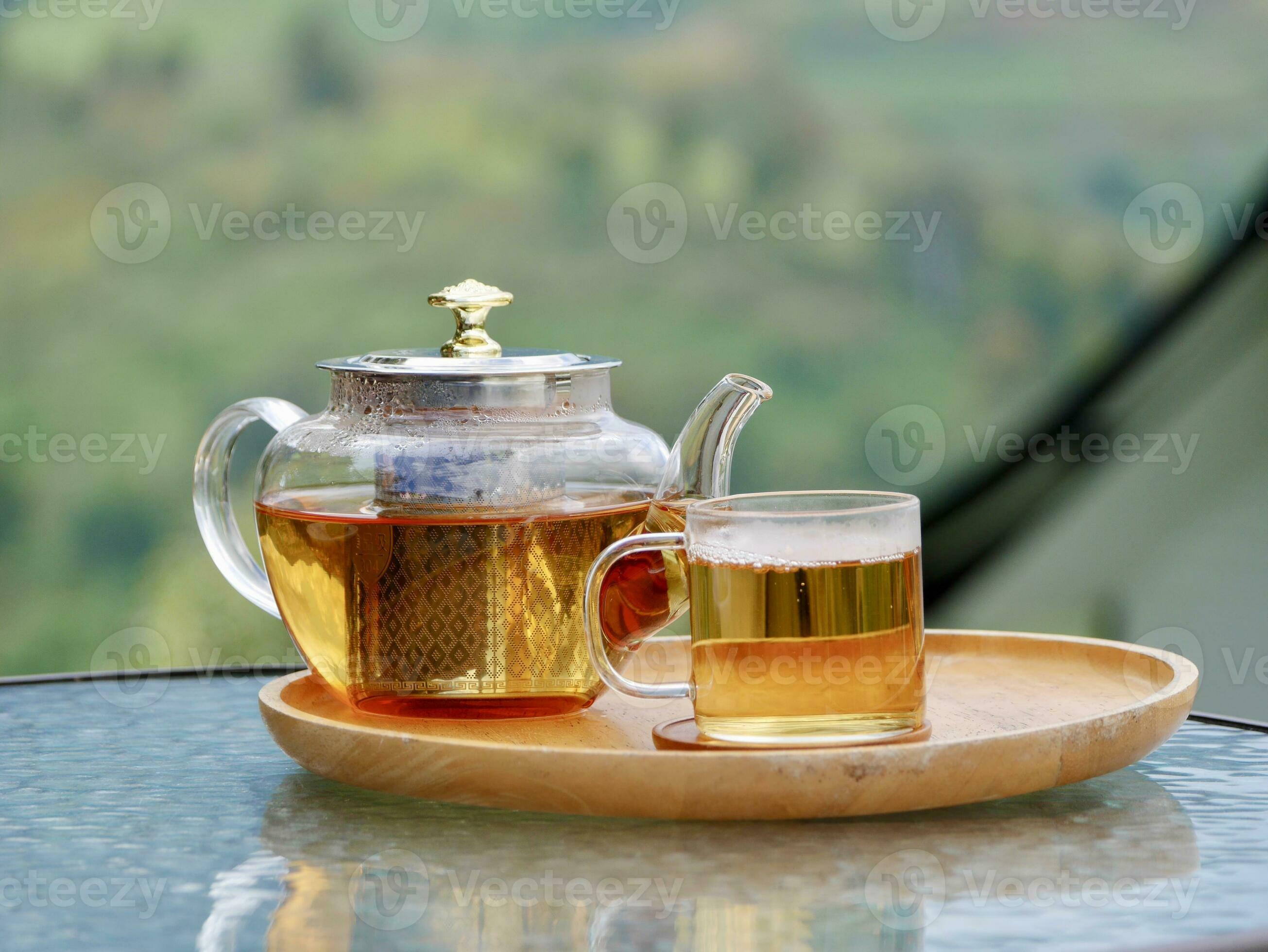 glass teapot on wooden serving tray, hands pouring tea from teapot