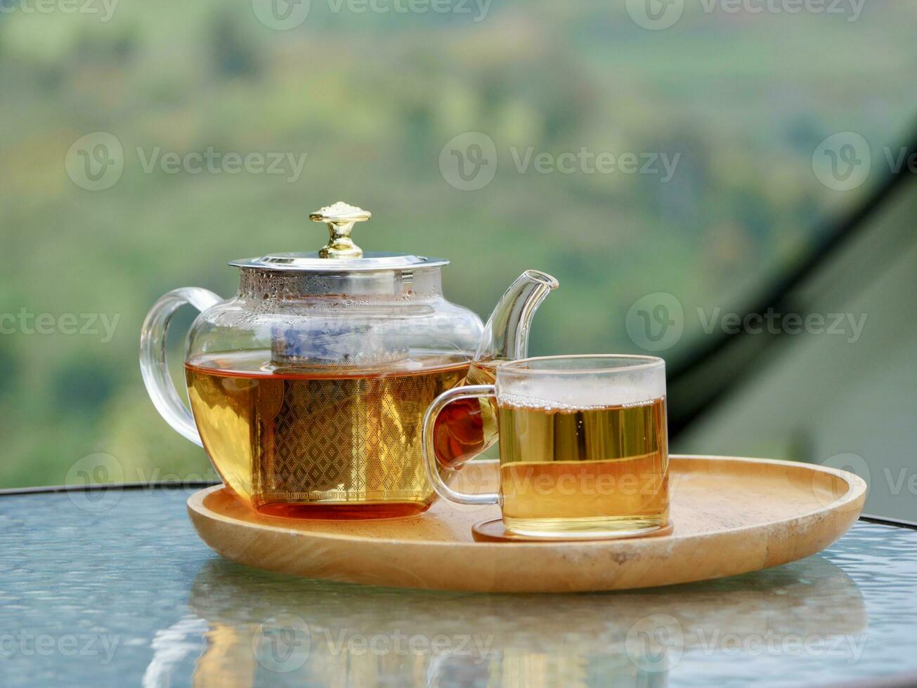 glass teapot on wooden serving tray, hands pouring tea from teapot, Cropped shot of pouring tea in traditional chinese tea ware photo