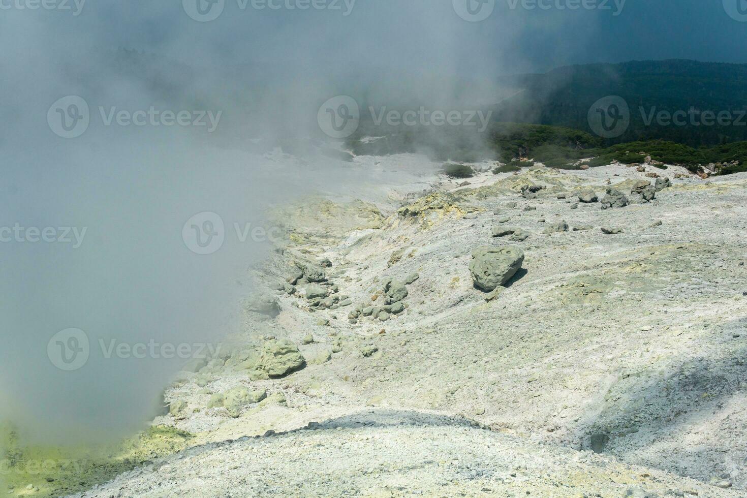 landscape of a fumarole field on the slope of a volcano is partially hidden by dense vapors photo