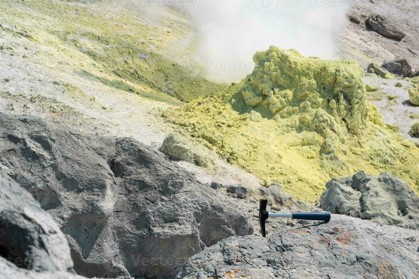geological hammer in the rock against the backdrop of an steaming fumarole on the slope of a volcano photo