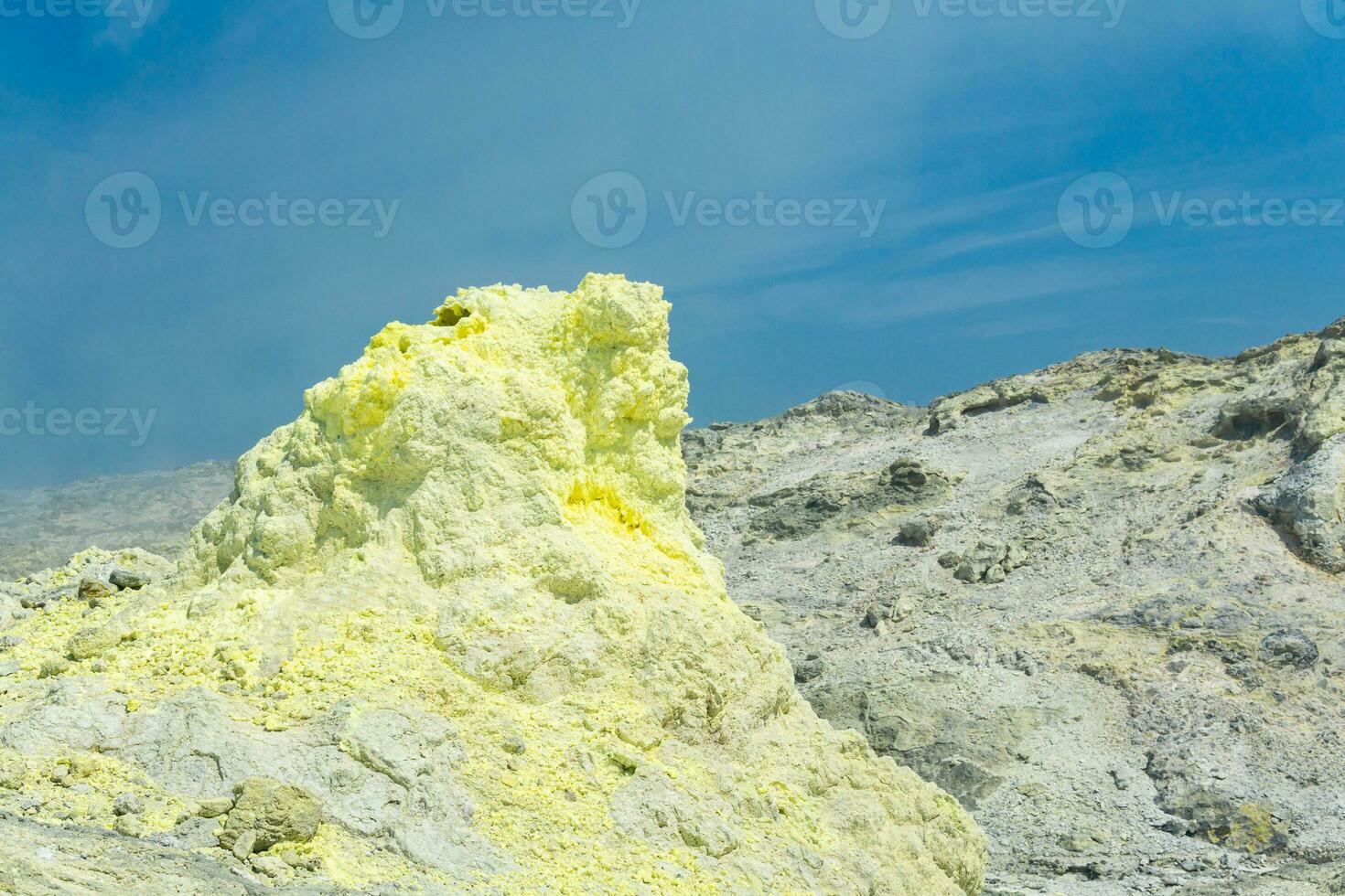 cone of sulfur deposits around a fumarole in a solfataric field against a blue sky photo