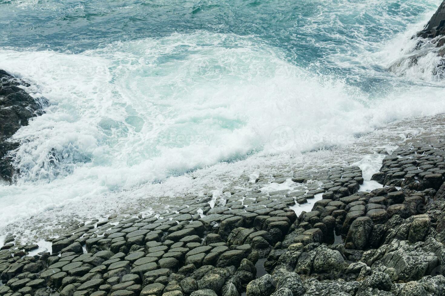 natural cobblestone causeway, formed by the ends of lava columns, descends into the sea surf photo