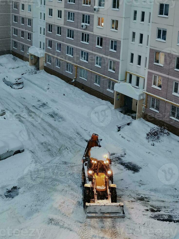 en el Mañana en el patio de un de muchos pisos edificio, un amarillo tractor borra el nieve, selectivo atención foto