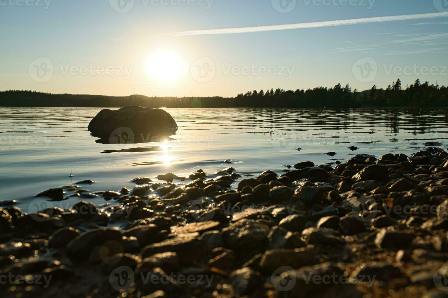 lago en suecia, pequeño y al atardecer con roca en primer plano de agua con bosque foto