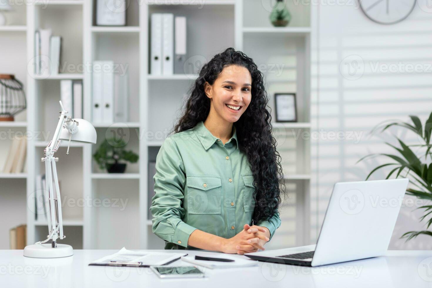 retrato de exitoso hermosa negocio mujer, Hispano mujer en hogar oficina sonriente y mirando a cámara, mujer a trabajo con ordenador portátil mecanografía en teclado. foto