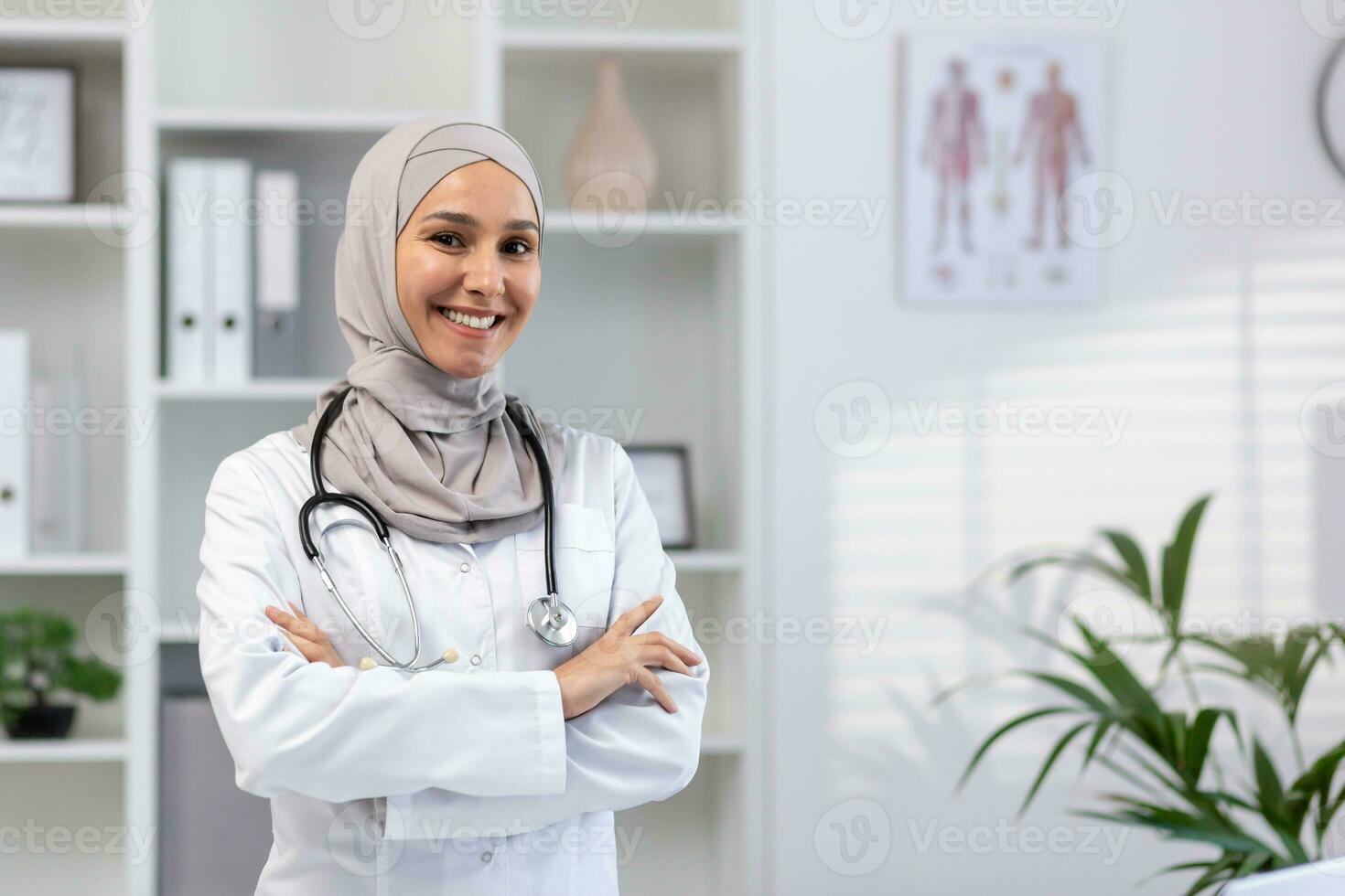 retrato de joven hembra médico vistiendo hiyab, musulmán mujer sonriente y mirando a cámara con brazos cruzado en blanco médico Saco con estetoscopio, trabajando dentro médico oficina oficina.. foto