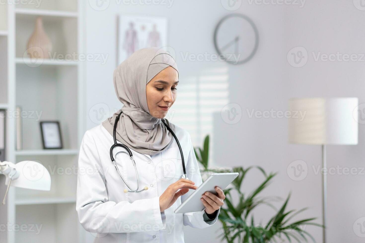 musulmán mujer en blanco médico Saco en pie dentro médico oficina de clínica, hembra médico utilizando tableta computadora pensando y concentrándose, concentrado mujer a trabajo en hospital foto
