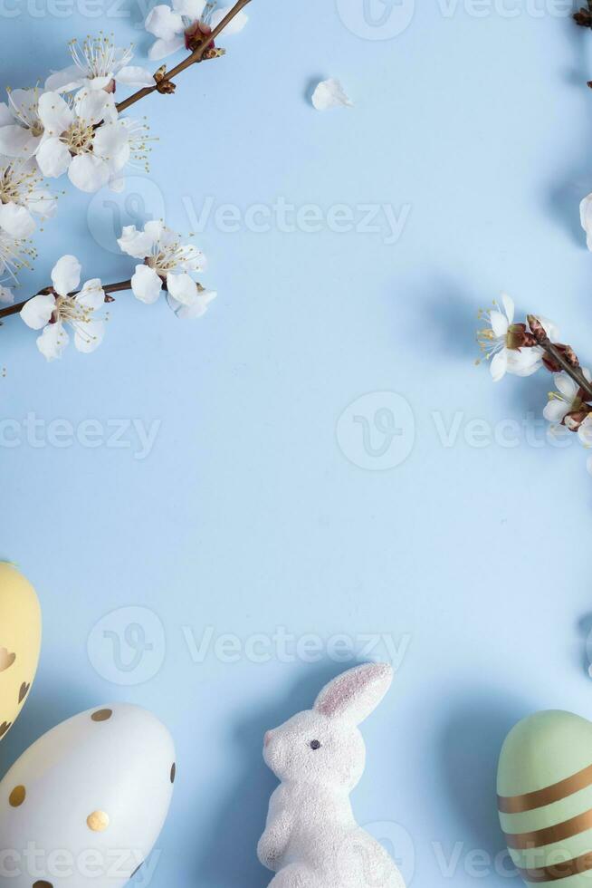 Easter eggs, rabbit and a flower branch on a blue background with copy space. photo